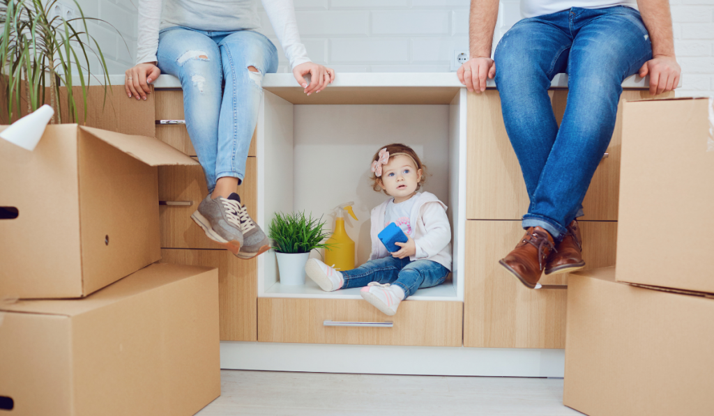 mom and dad sitting in the kitchen counter with their cute toddler sitting in an open space of the cabinet