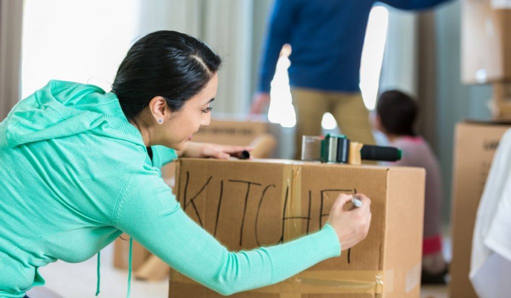 girl labeling the box of kitchen items