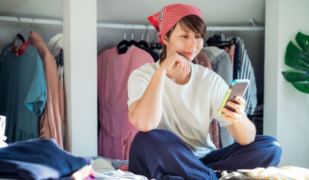 girl sitting down browsing her phone and sorting her clothes