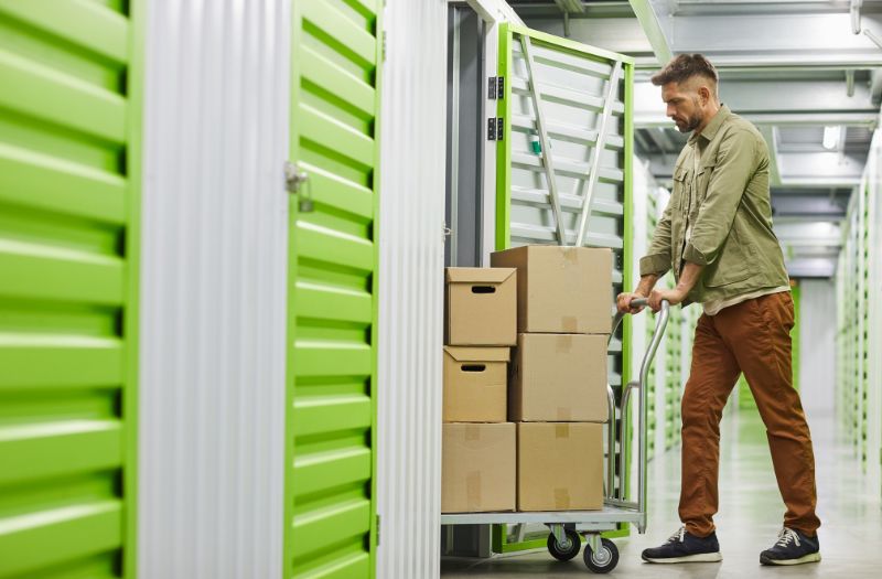 man pushing a cart of boxes in a storage unit to keep